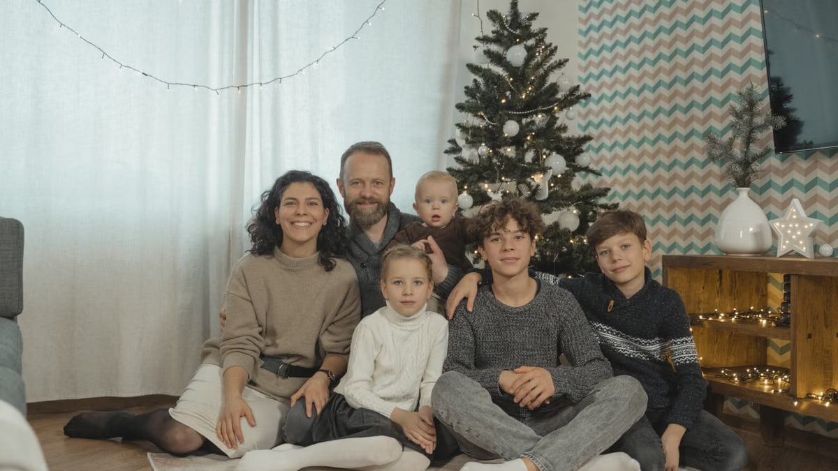 A family posing cheerfully indoors next to a Christmas tree.